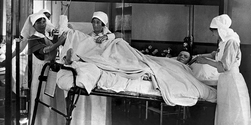 black and white historical image of nurses supporting a patient around his bed