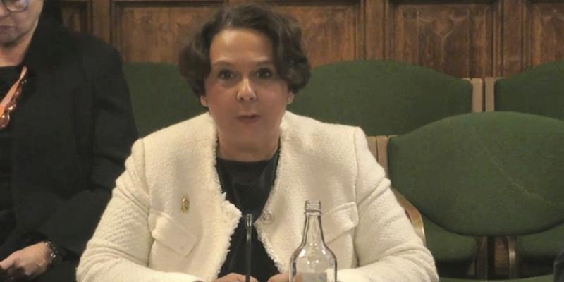 Royal College of Nursing General Secretary and Chief Executive Professor Nicola Ranger gives evidence at the Health and Social Care Select Committee in Parliament. She is wearing a white cardigan over a black top and is seated with green chairs and wood paneling seen behind her.