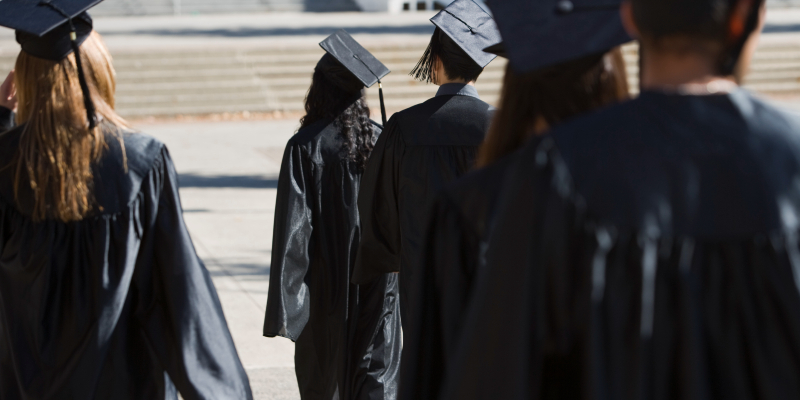 Photo shows students wearing black university graduation robes and caps walking away from camera 