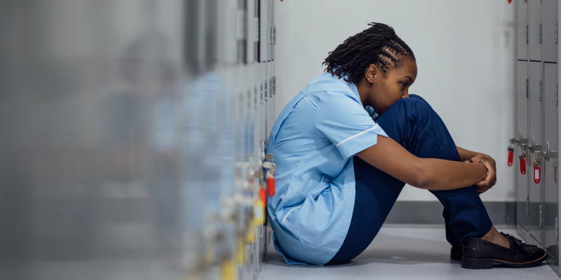 Nurse in uniform sits with back against lockers and head against knees